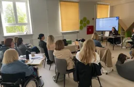 nauczyciele słuchaja wykładu w tle prowadzący i tablica multimedialna