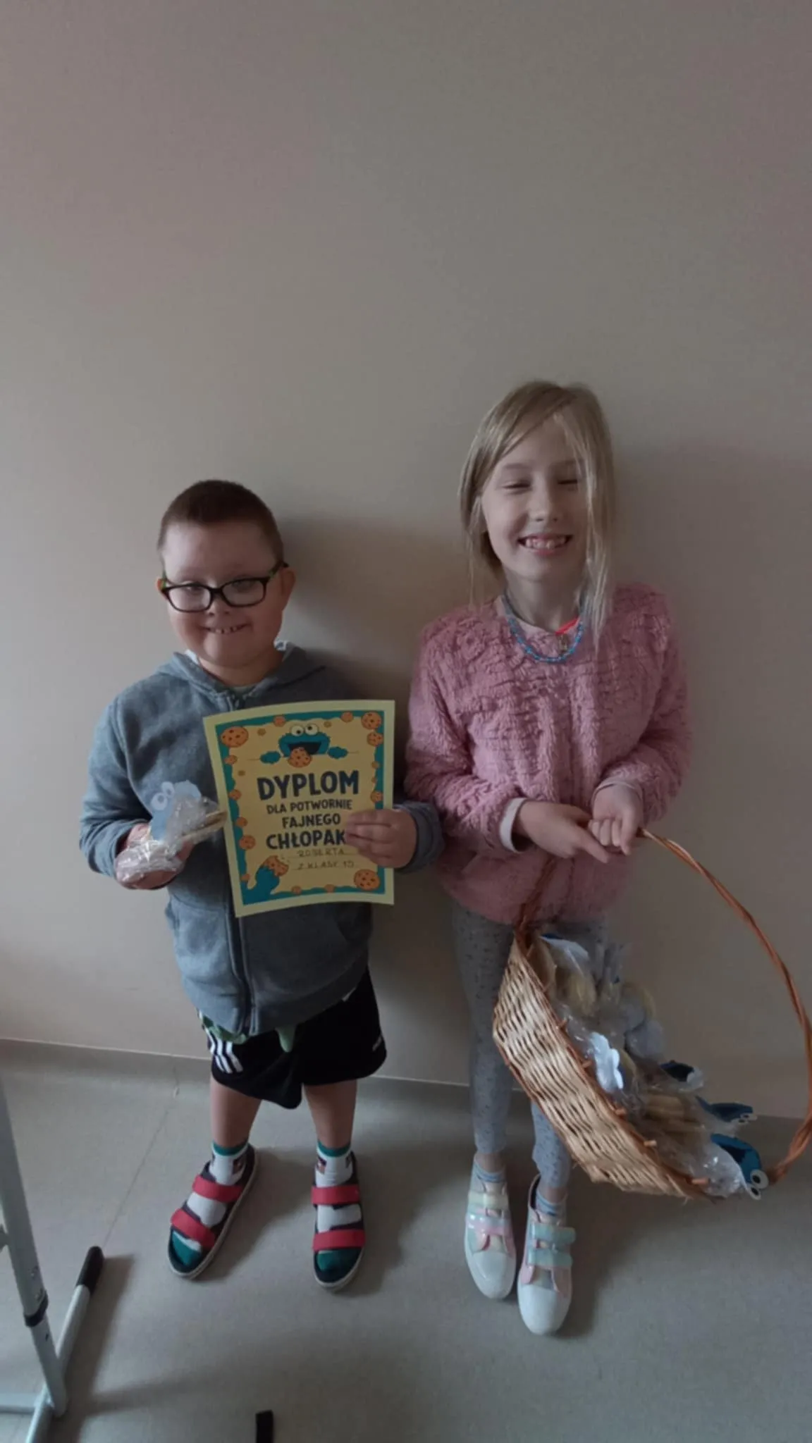Przewodnicząca SU Roksana stoi  obok kolegi, w ręku trzyma koszyk z prezentami. kolega trzyma w ręku dyplom. 