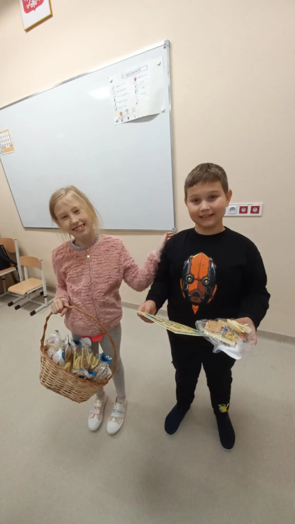 Przewodnicząca SU Roksana stoi  obok kolegi, w ręku trzyma koszyk z prezentami. Kolega trzyma w ręku  prezent. 