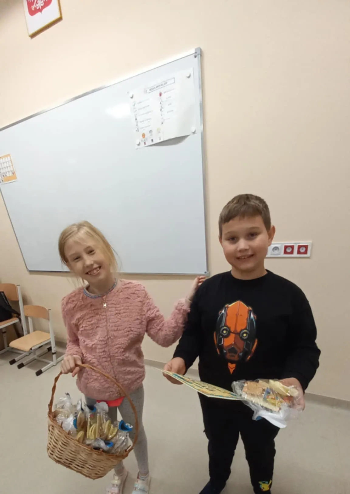 Przewodnicząca SU Roksana stoi obok kolegi, w ręku trzyma koszyk pełen prezentów. Kolega ma w ręku prezent, który dostał z okazji Dnia Chłopaka