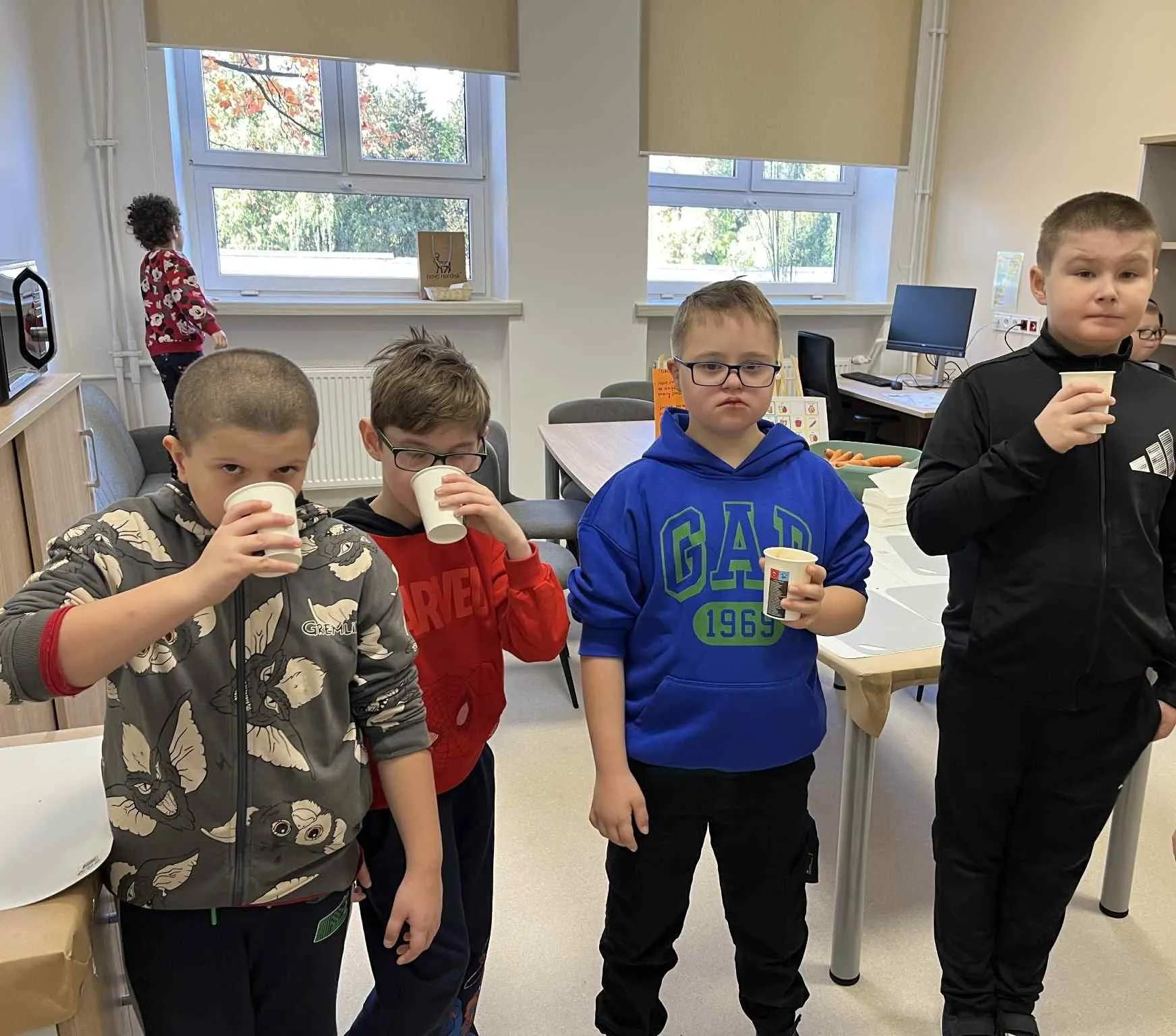 Trzech chłopców stoi z kubeczkami w ręku i piją świeżo zrobiony sok