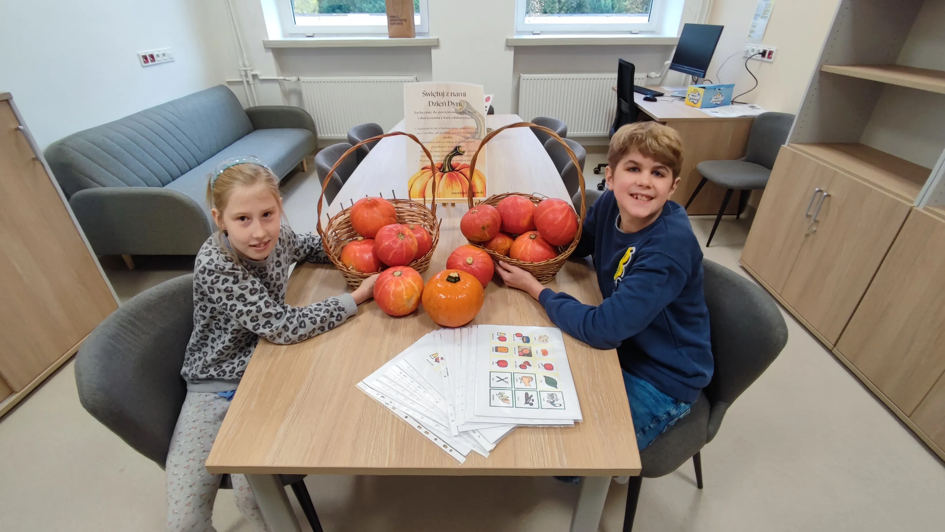 Na zdjęciu widzimy dwoje uczniów siedzących przy stole,  Dzieci prezentują kosze z dyniami.