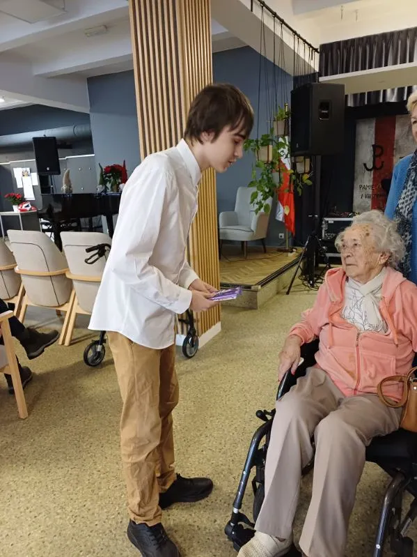 Uczeń wręcza kartkę świąteczna uczestniczce Powstania Warszawskiego w Domu Powstańców  Warszawskich