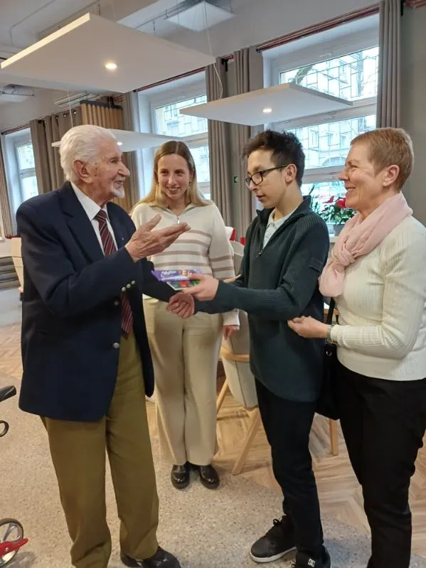 Uczeń wraz z towarzyszącą mu wychowawczynią wita się z jednym z powstańców w Domu Powstańców Warszawskich