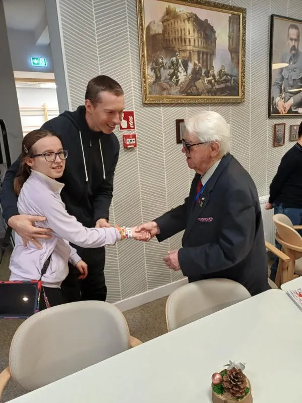 Uczennica wraz z towarzyszącym jej nauczycielem wita się z jednym z powstańców  w Domu Powstańców Warszawskich