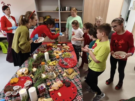 Do stołu pełnych łakoci  (wypieki i owoce) podchodzą uczniowie oraz osoby dorosłe z zamiarem  częstowania się  smakołykami ze stołu.