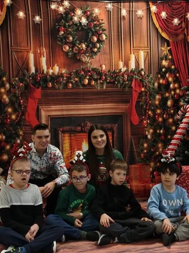 Pamiątkowe zdjęcie: czworo uczniów z nauczycielką i pomocnikiem nauczyciela pięknie prezentują się na tle ścianki  fotograficznej przybranej w akcesoria  Bożonarodzeniowe: łańcuchy, bombki, stroiki,  świece.