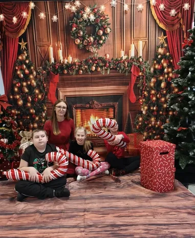 Pani wychowawczyni z kl. 3b z dwojgiem swoich uczniów na tle ścianki fotograficznej udekorowanej stroikami, bombkami, łańcuchami, swicami.