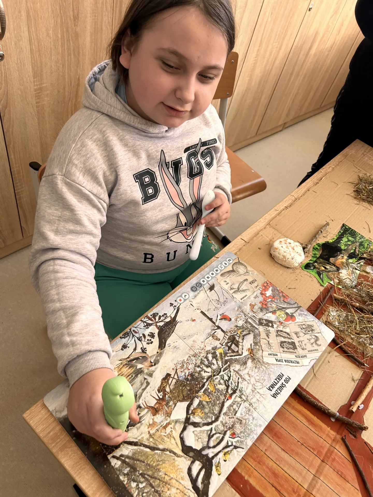 Uczennica przy ćwiczeniu polegającym na wyszukiwaniu informacji przy pomocy pióra elektronicznego , którym jeździ po  "leśnej" macie