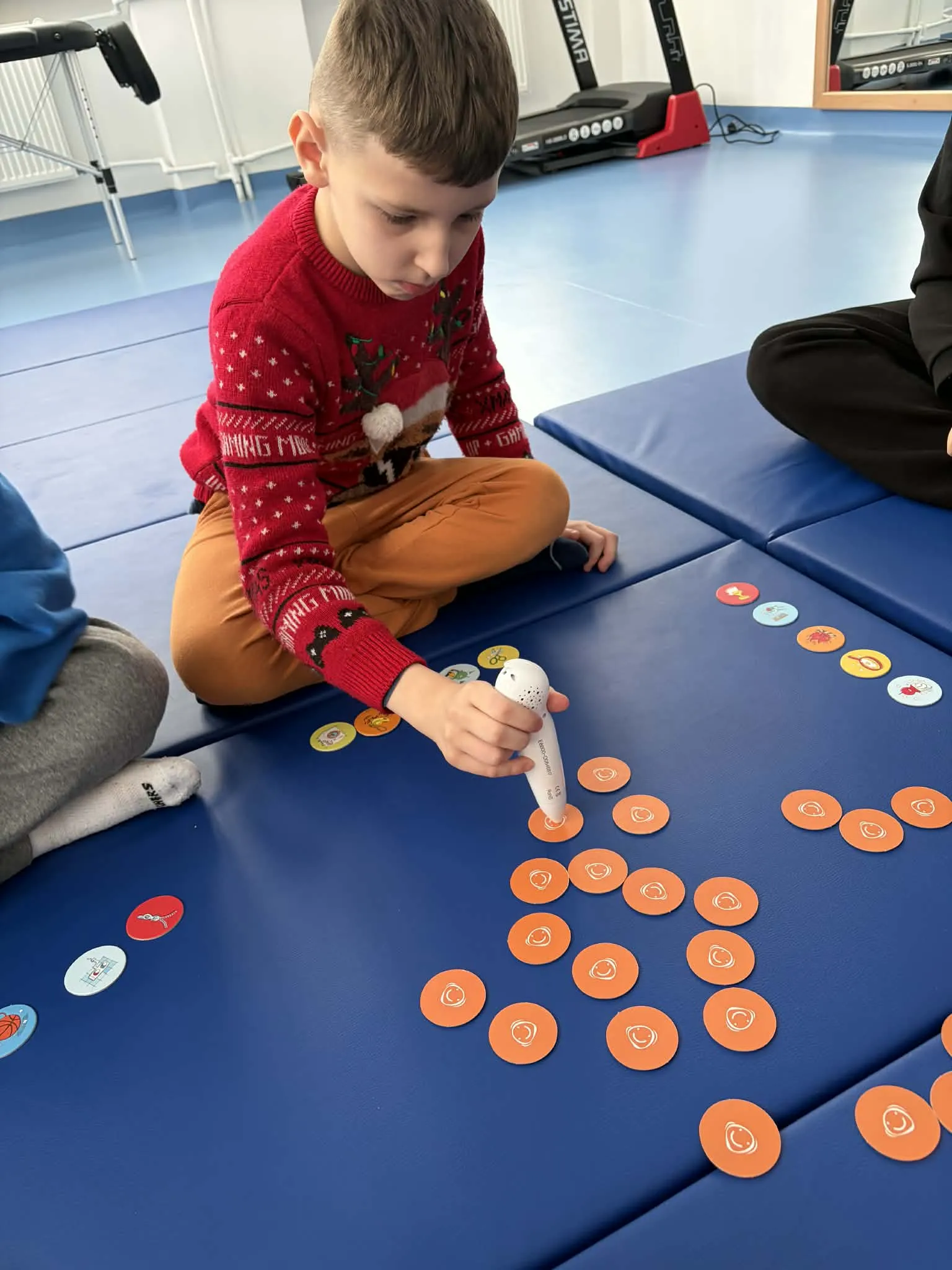 Uczeń przy pomocy pióra elektronicznego odtwarza dźwięki dotykając  leżących na kartonie krążków