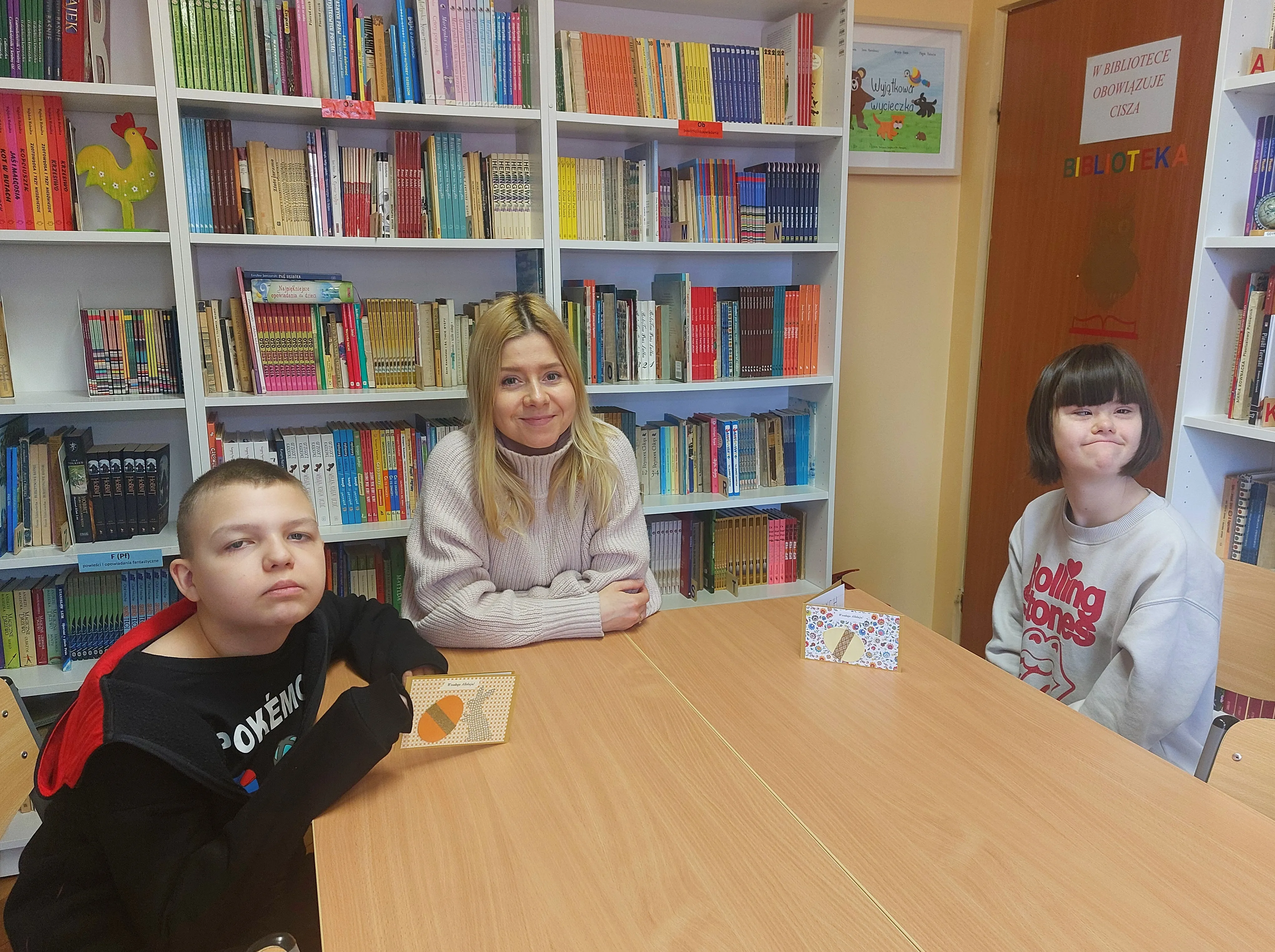 Dwoje uczniów klasy 6e (wraz z  wychowawczynią) prezentują w bibliotece szkolnej kartki świąteczne