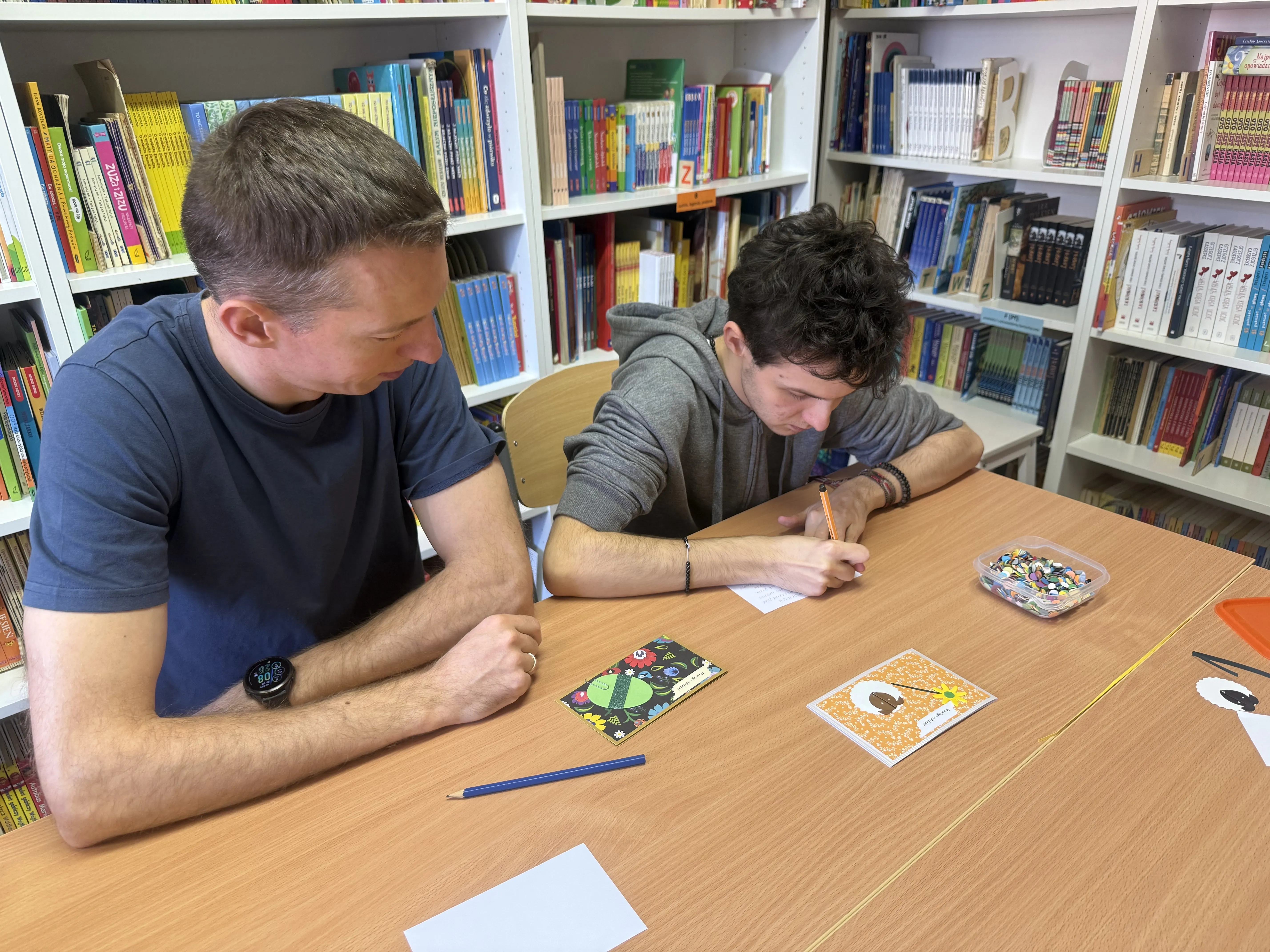 Uczeń klasy 8c( wraz z nauczycielem rehabilitacji) w bibliotece szkolnej -  wykonuje kartkę świąteczną