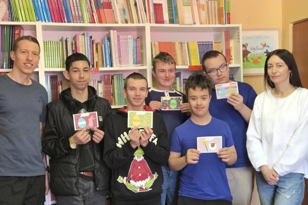 Uczniowie klasy 8c prezentują w bibliotece szkolnej kartki świąteczne. Obok uczniów stoi wychowawczyni oraz nauczyciel rehabilitacji