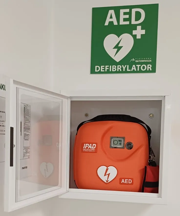 Zdjecie przedstawia otwartą skrzynkę na ścianie z urzadzeniem AED