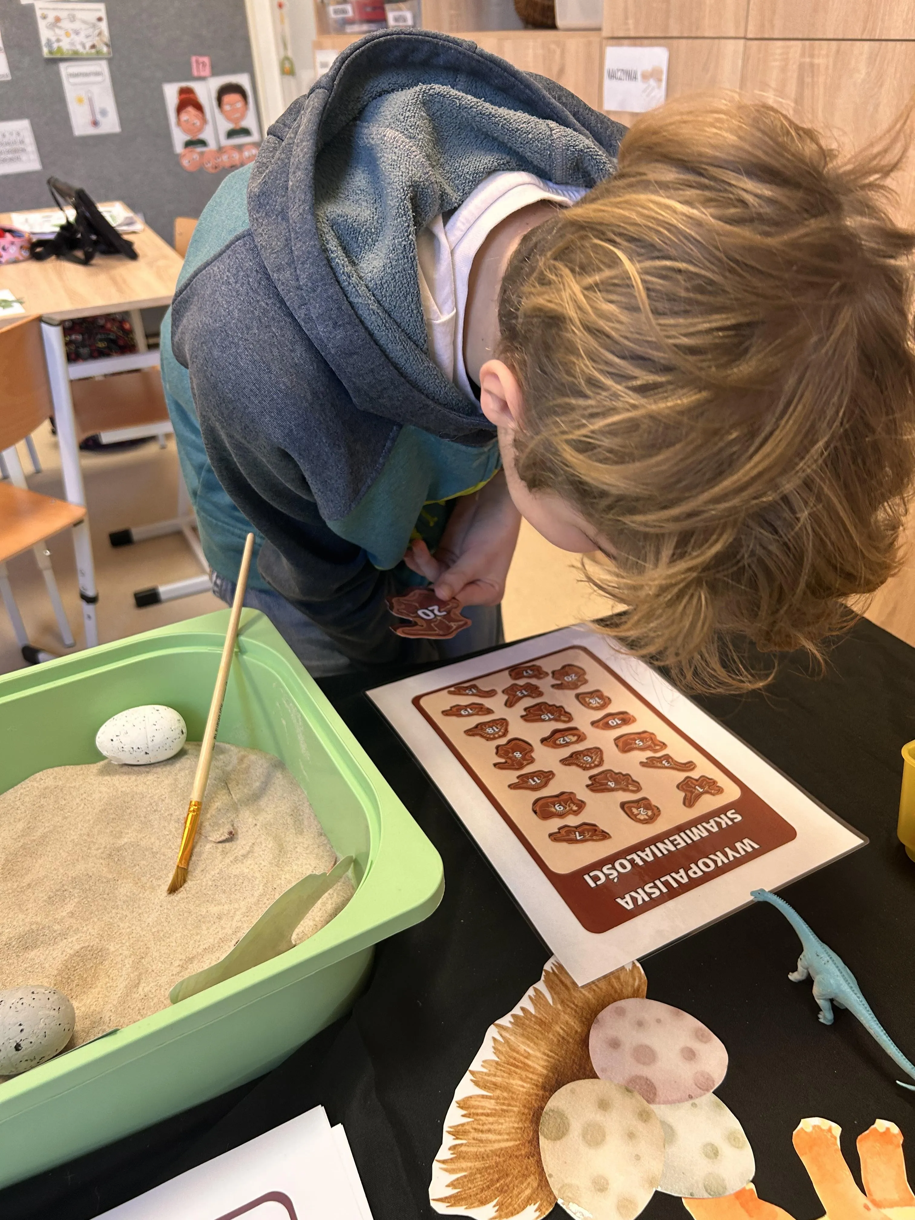 Na zdjęciu uczeń pochylony nad planszą  przedstawiającą wykopaliska