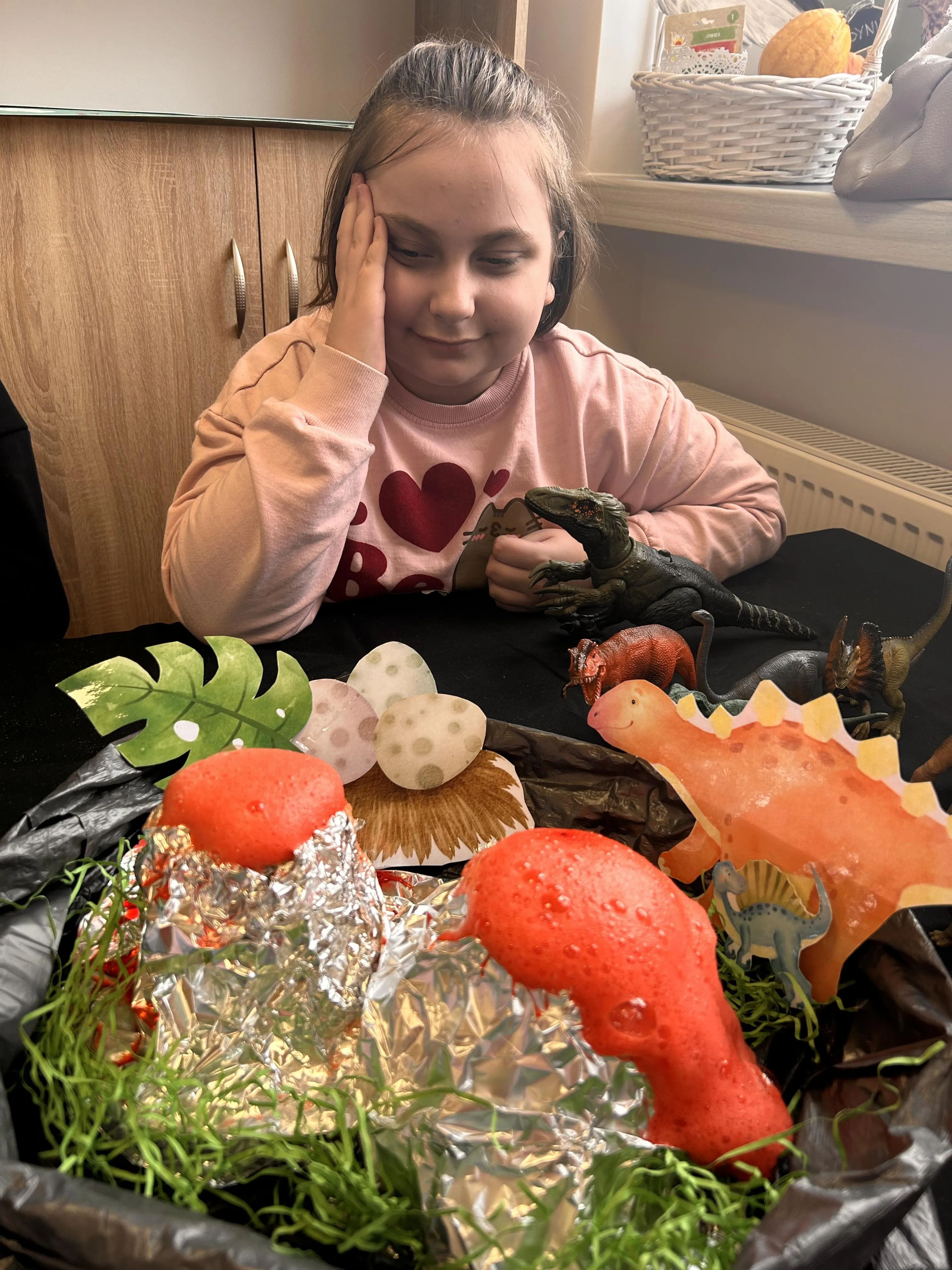 Uczennica siedzi przy stoliku, ogląda akcesoria związane z dinozaurami