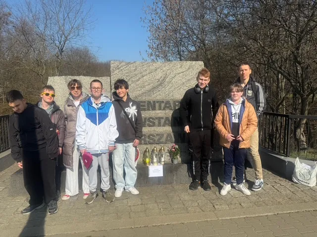 Pamiątkowe zdjęcie grupy uczniów z dwojgiem nauczycieli  - przy płycie głównej Cmentarza Powstańców Warszawy.