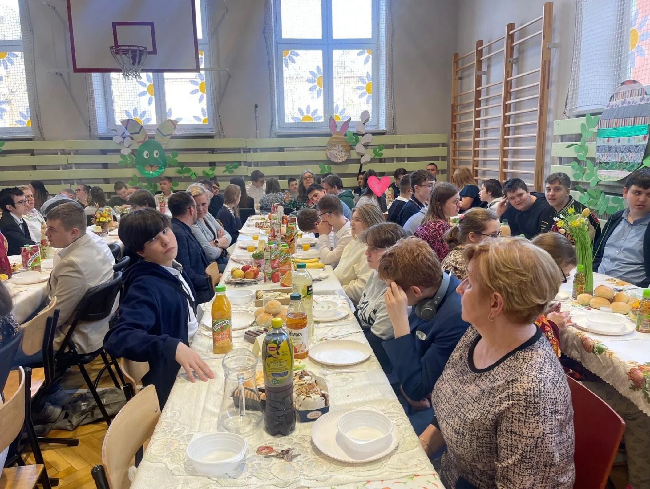 uczniowie i nauczyciele siedzacy przy stołach w sali gimnastycznej przy śniadaniu wielkancnym