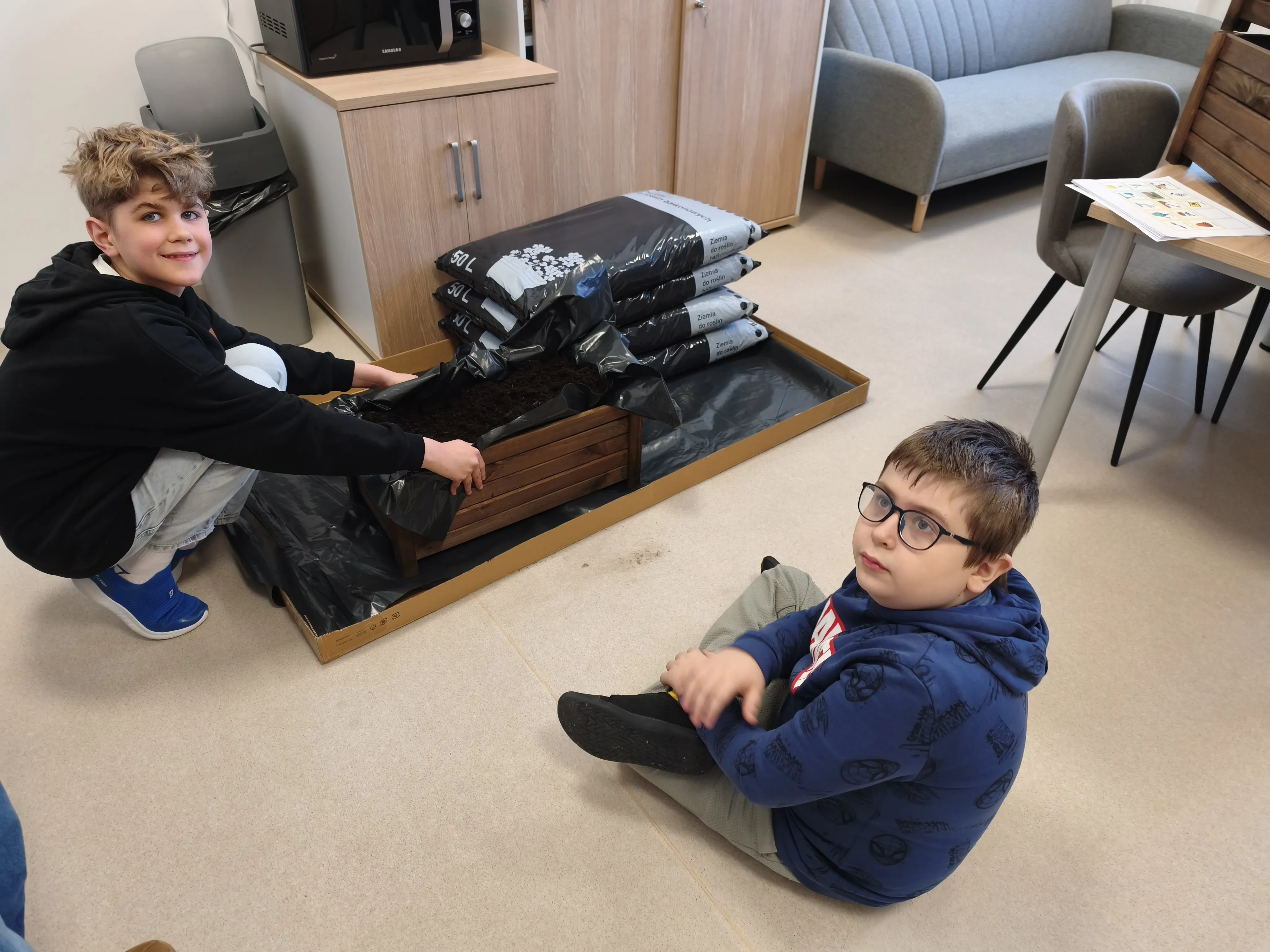 chłopcy kleczą przy donicach