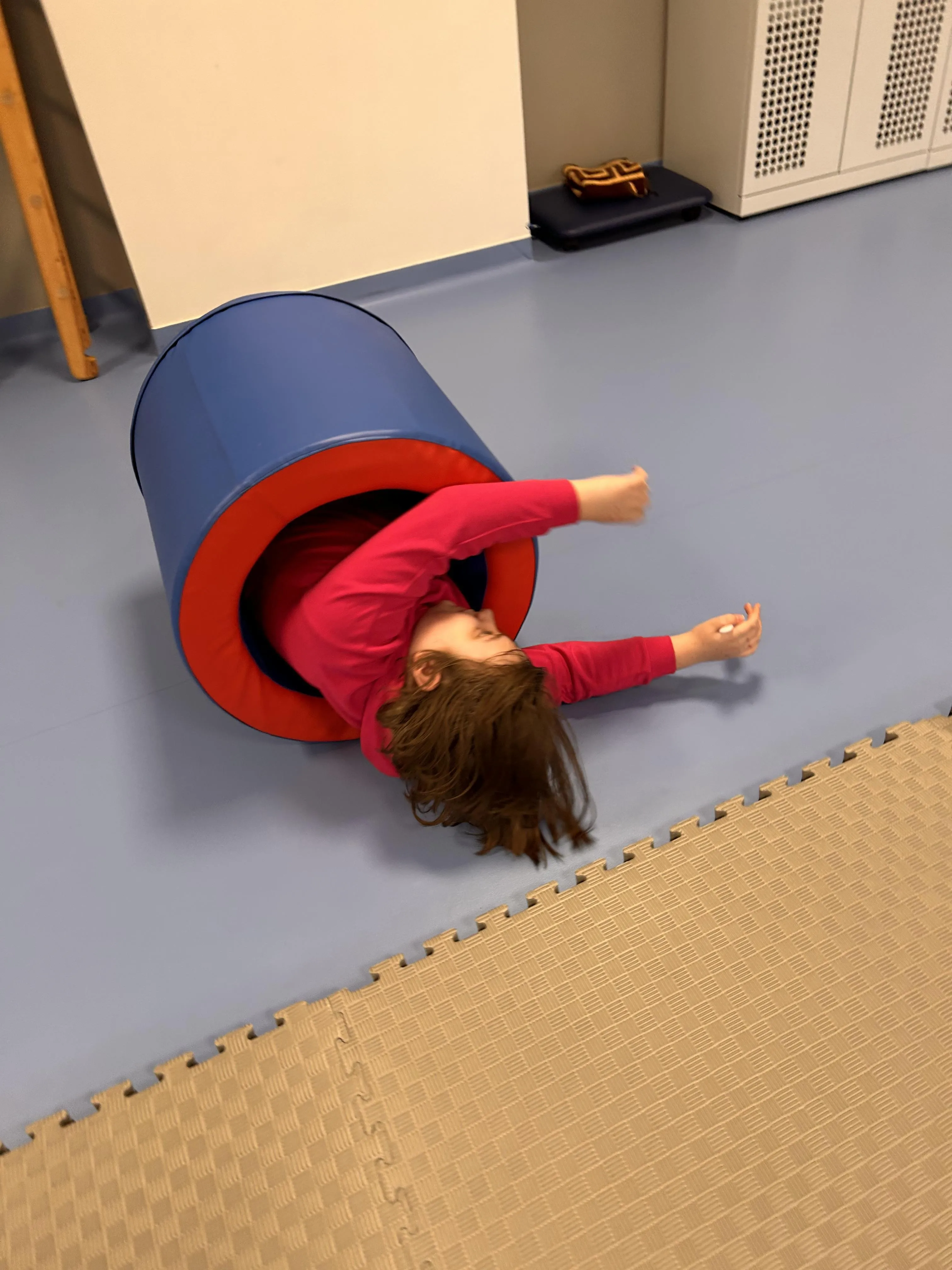 Na zdjęciu - leżąca na rozłożonym na szkolnym korytarzu dywaniku uczennica, która turla się po podłodze w  gumowym pierścieniu.