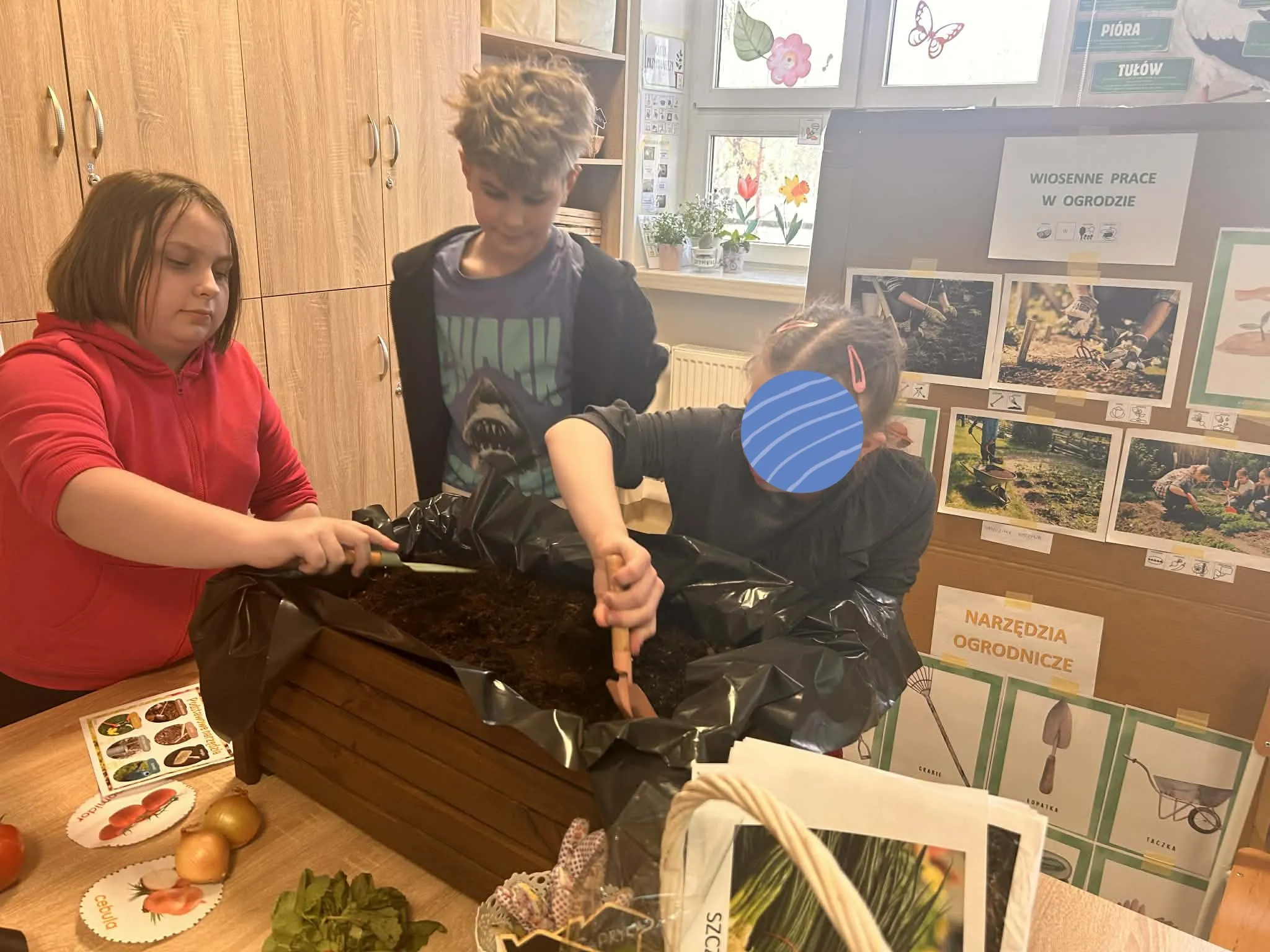 dwie dziewczynki i chłopiec sadzą rosliny w donicy