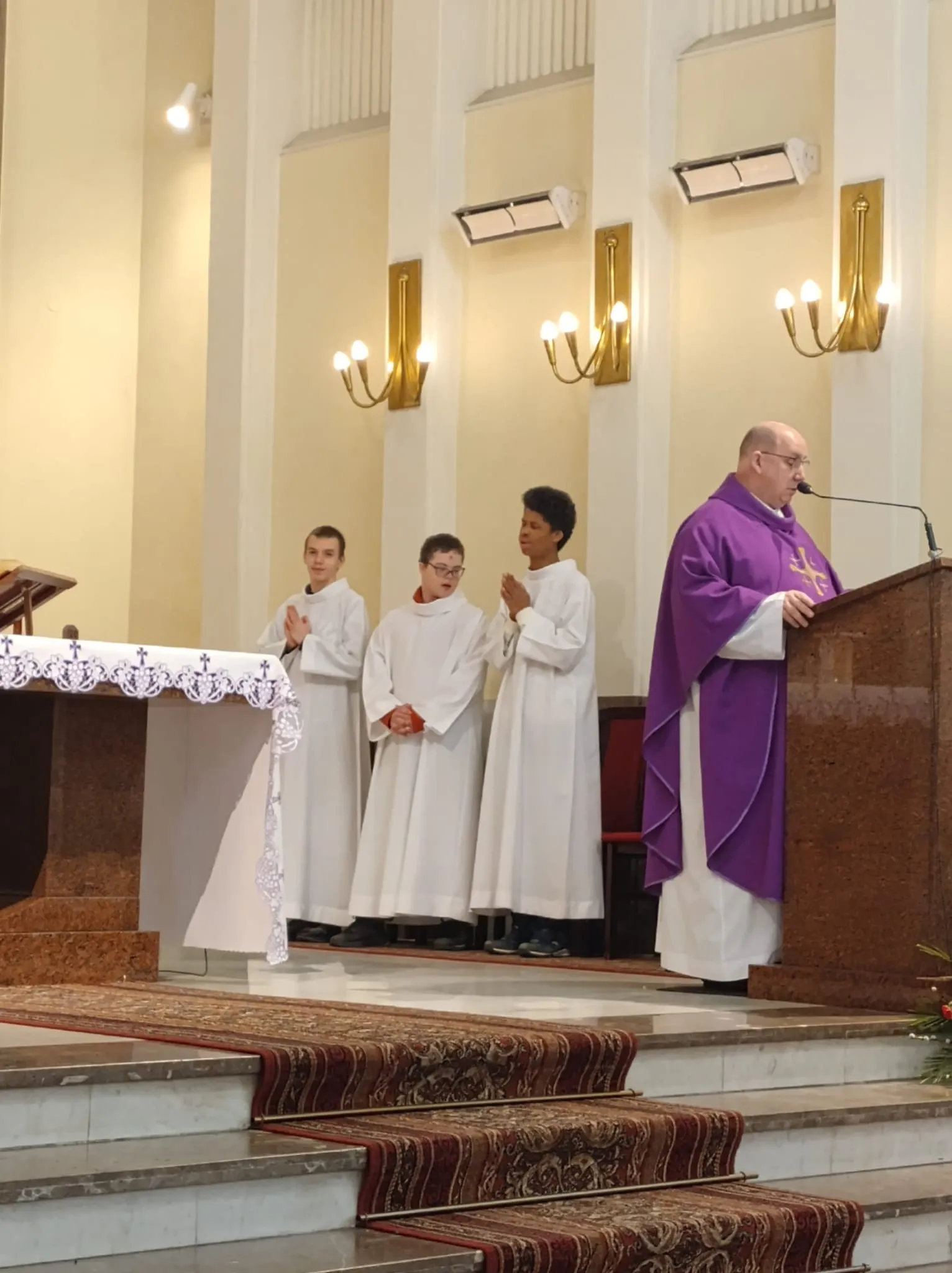 ksiadz stojacy przy ambonie w tle ministarnci ze szkoły SPS nr 147