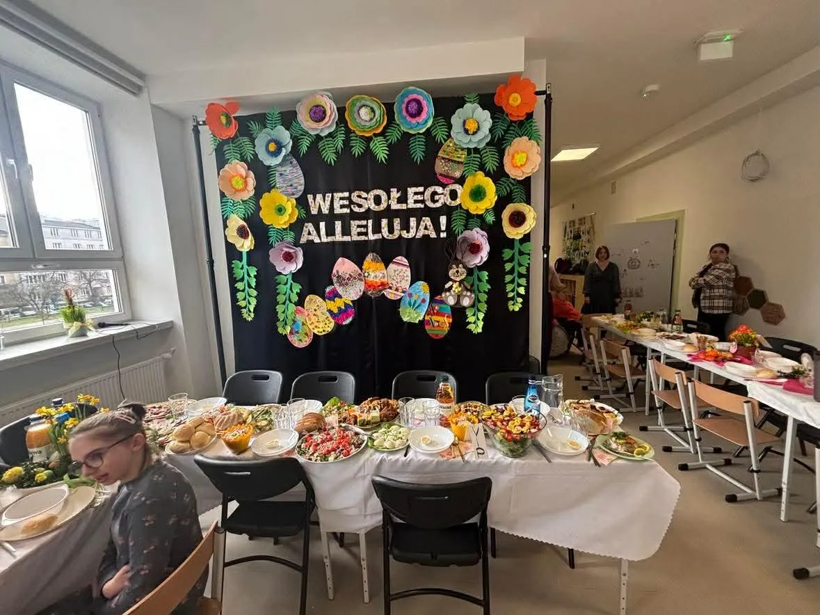 uczniowie i nauczyciele siedzacy przy stołach w sali gimnastycznej przy śniadaniu wielkancnym