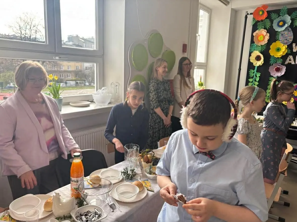 uczniowie i nauczyciele siedzacy przy stołach w sali gimnastycznej przy śniadaniu wielkancnym