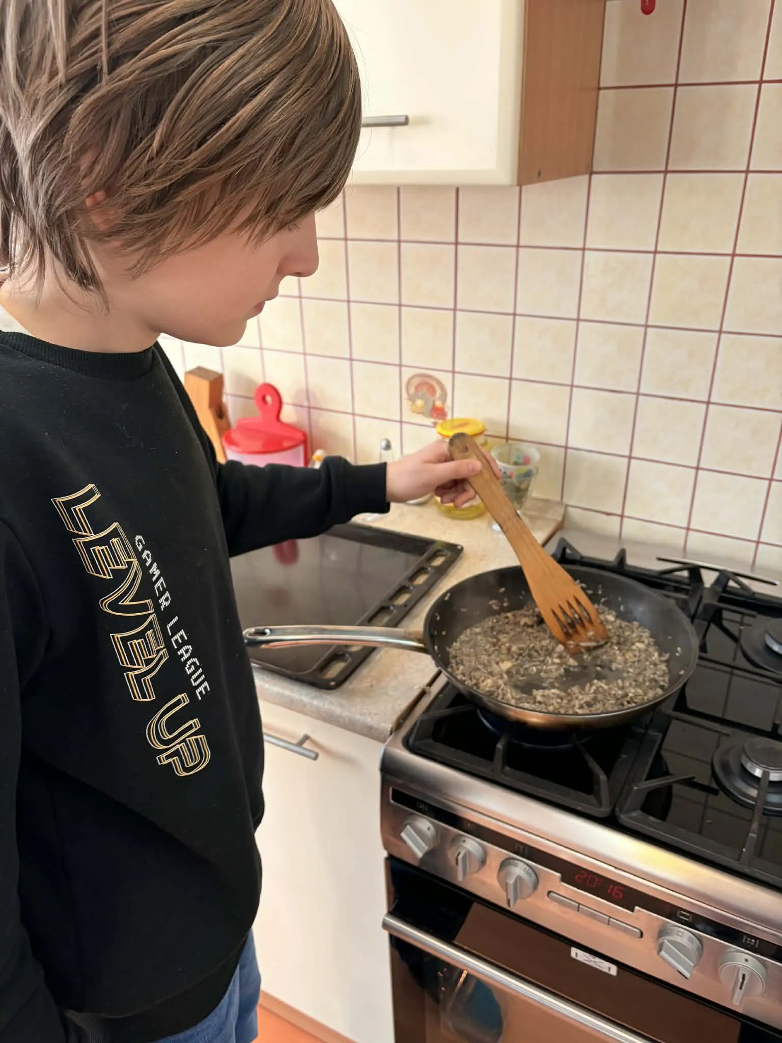 na zdjęciu  - uczeń w pomieszczeniu gospodarczym, stoi przy kuchence i miesza na patelni pokrojone drobno pieczarki