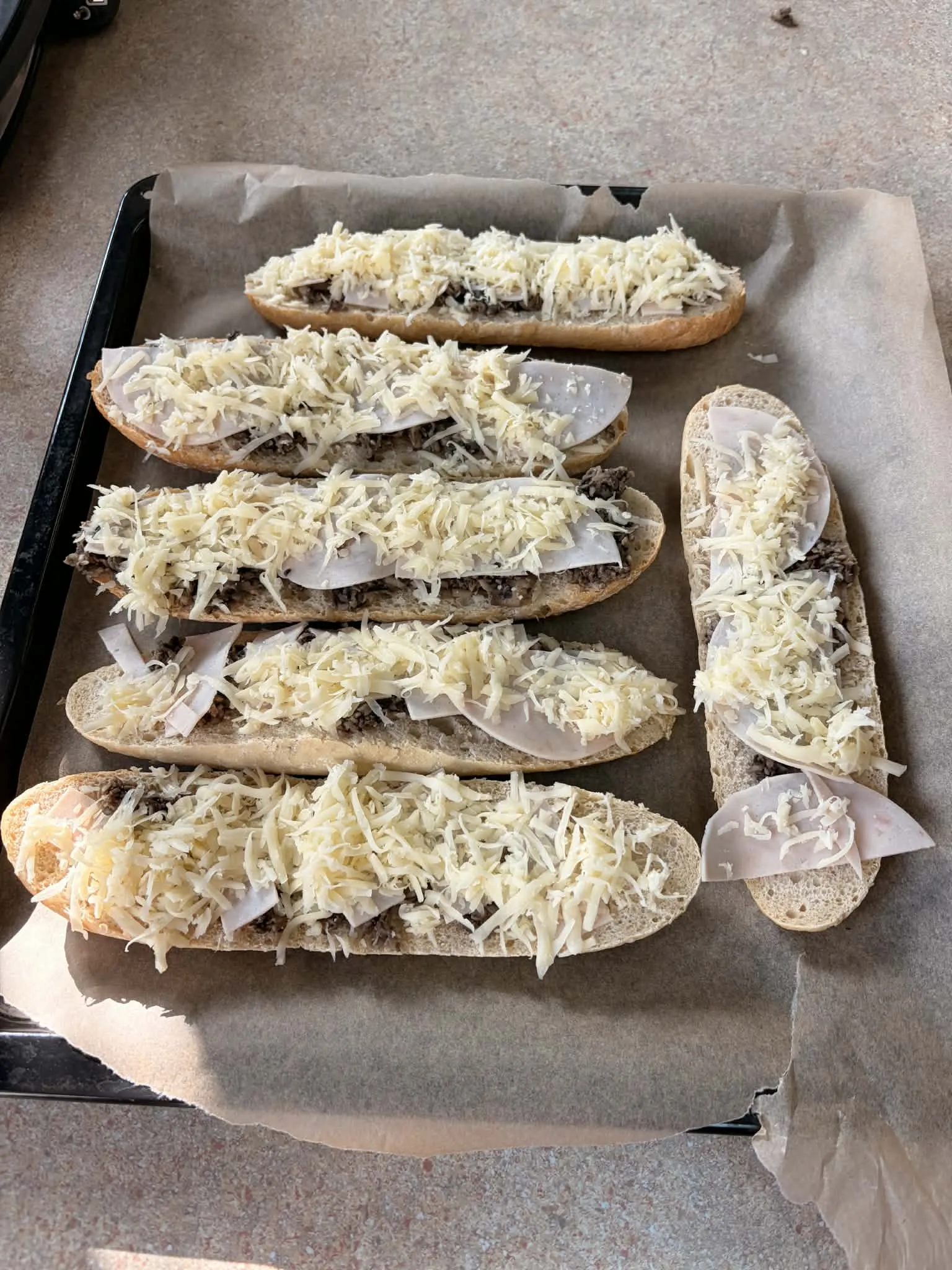 Na zdjęciu - sześć leżących na blasze z piekarnika  zapiekanek posypanych złotym serem