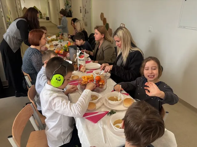 Na  zdjęciu widoczny jest , stojący na korytarzu szkolnym świąteczny stół  i  siedzący  nich uczniowie, nauczycielami  i  połonicznikami  nauczycieli