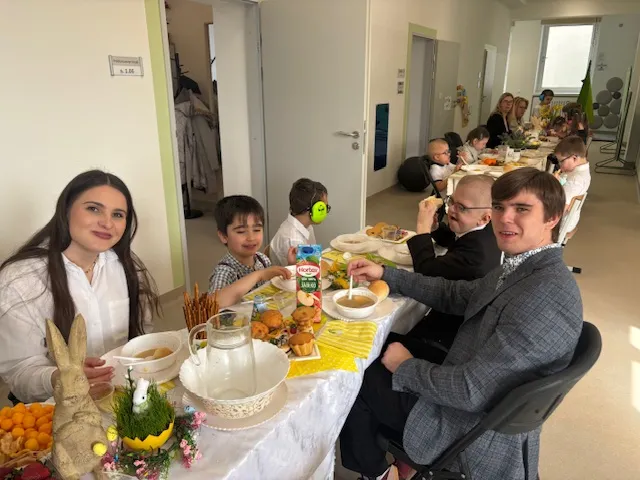 Na  zdjęciu widoczne są dwa , stojące na korytarzu szkolnym świąteczne stoły  i siedzącymi  przy nich uczniami, nauczycielami  i  połonicznikami  nauczycieli