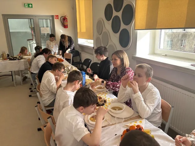 W centralnej części zdjęcia  - widoczny świąteczny stół oraz siedzący przy nim uczniowie i nauczyciele