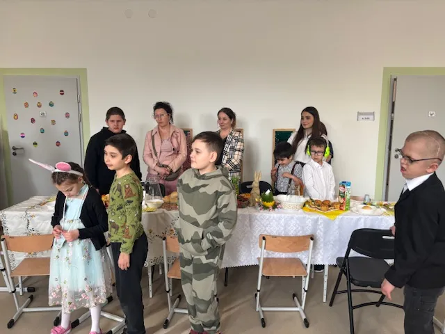 W centralnej części zdjęcia widoczny jest świąteczny stół i stojący przy nim uczniowie i nauczyciele