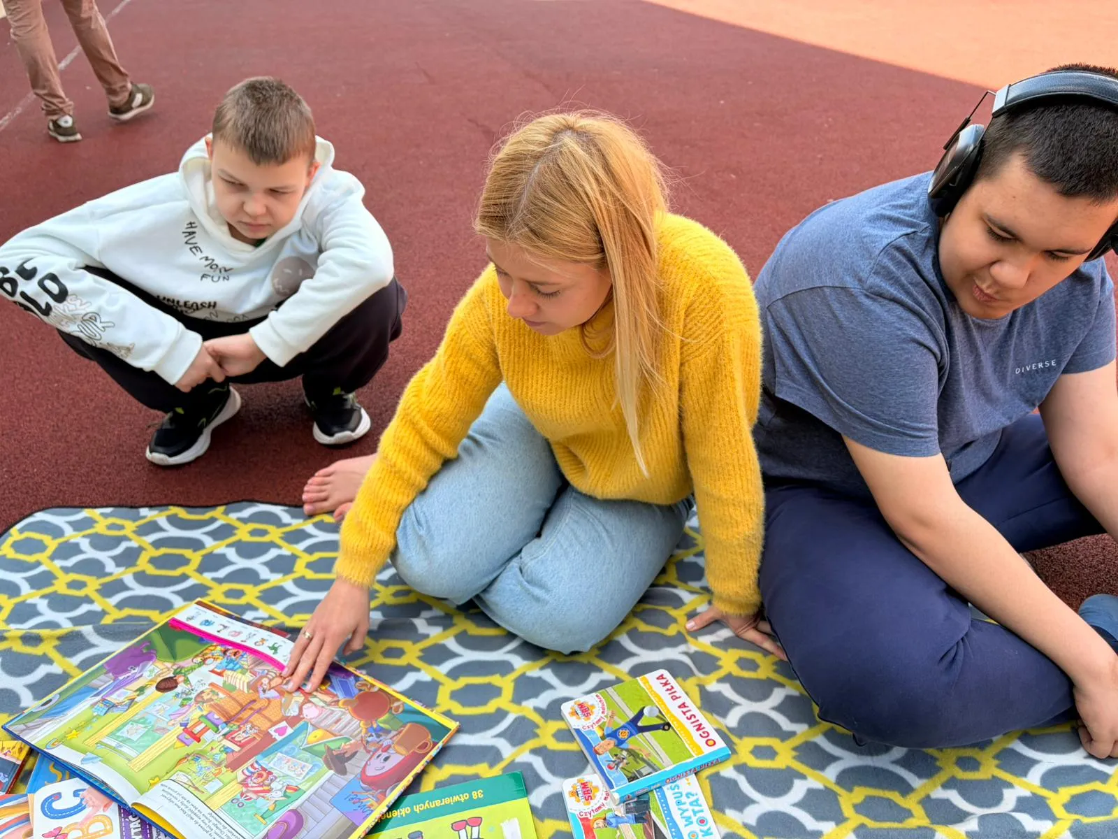 uczniowie siedzą na boisku szkolnm z ksazkami
