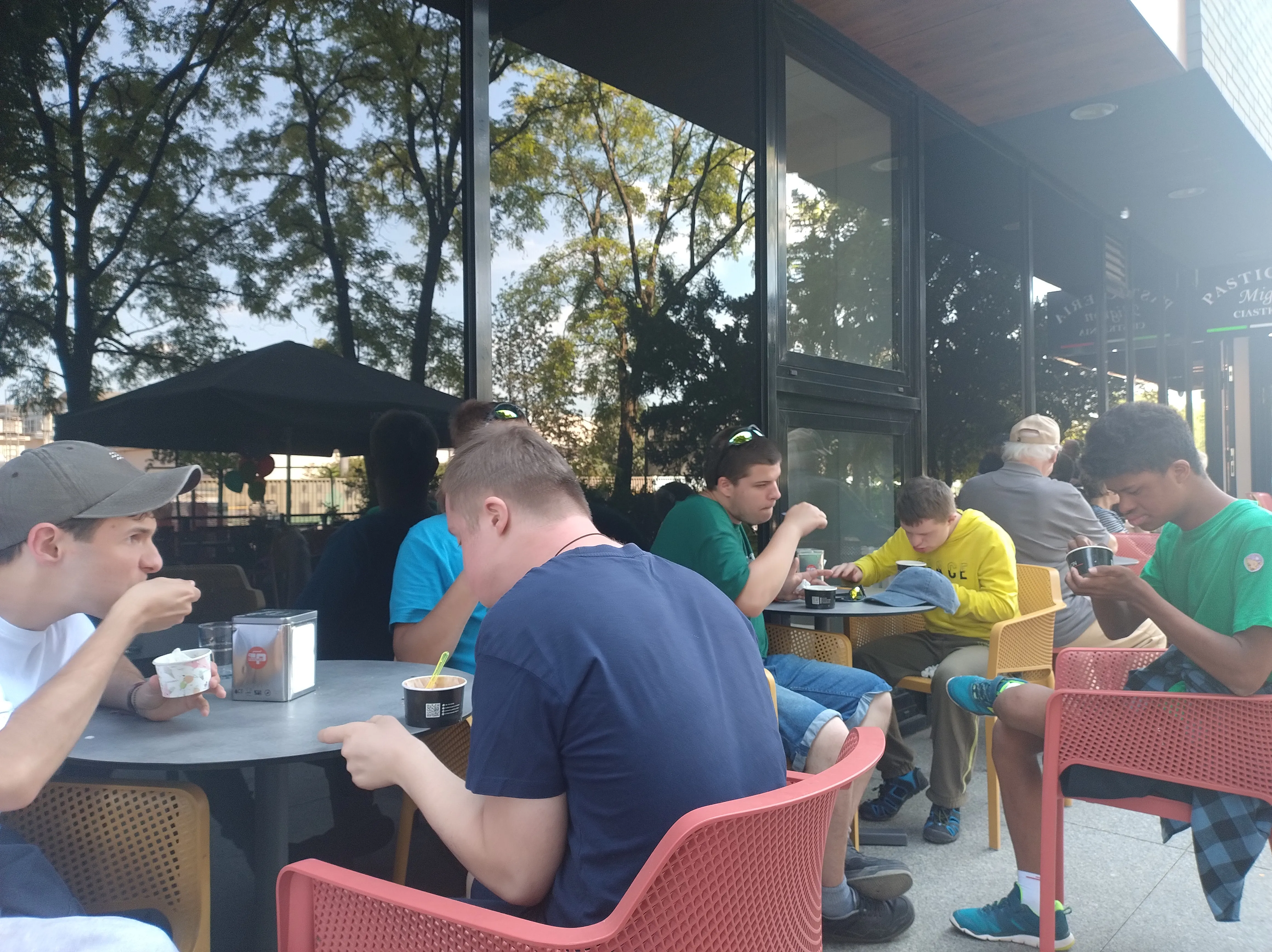 Na zdjęciu uczniowie siedzący przed barem restauracyjnym - jedzą lody.
