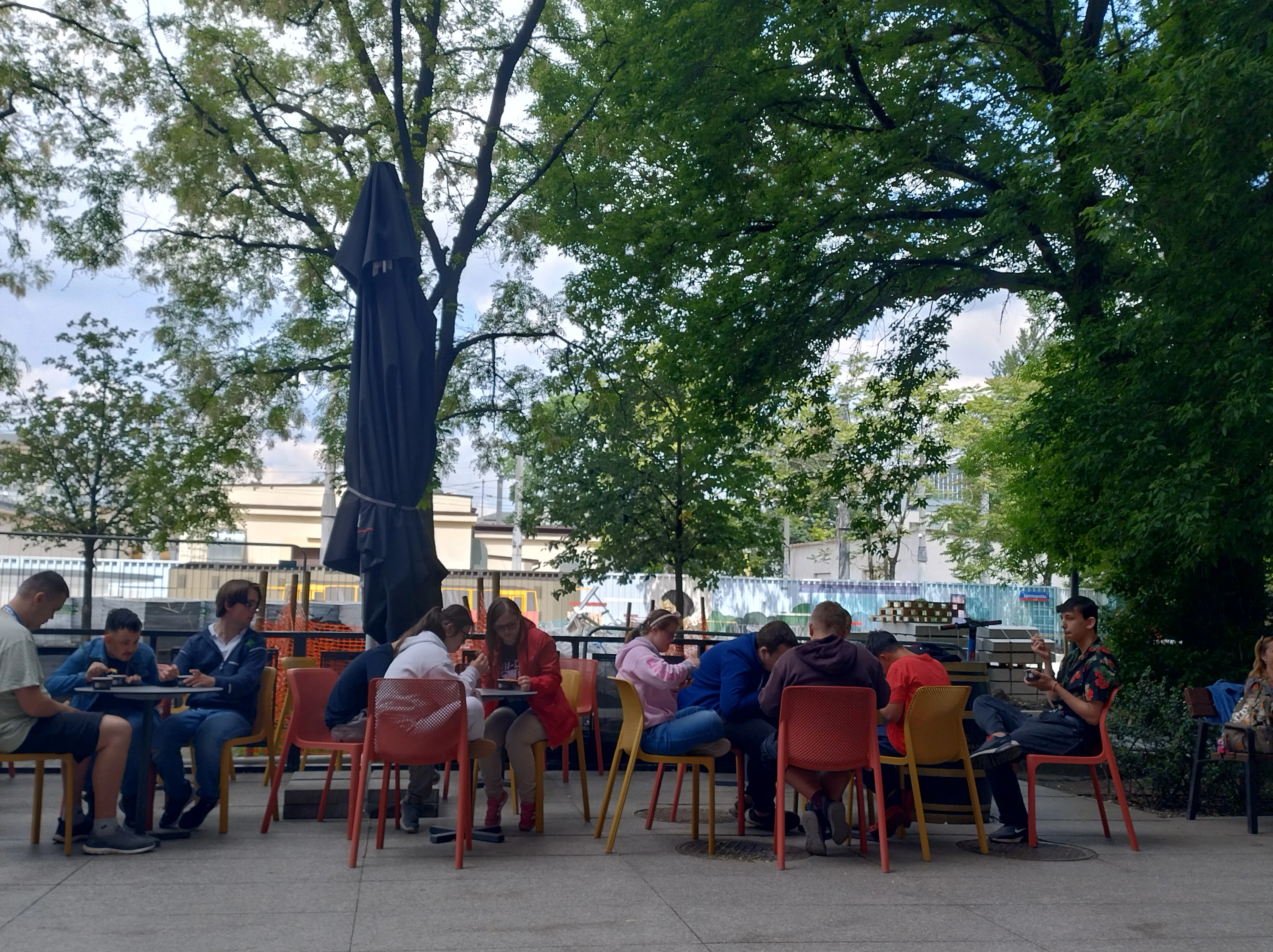 Na zdjęciu widoczne są 3 stoliki przy barze restauracyjnym.  Wokół stolików siedzą uczniowie i  jedzą lody.