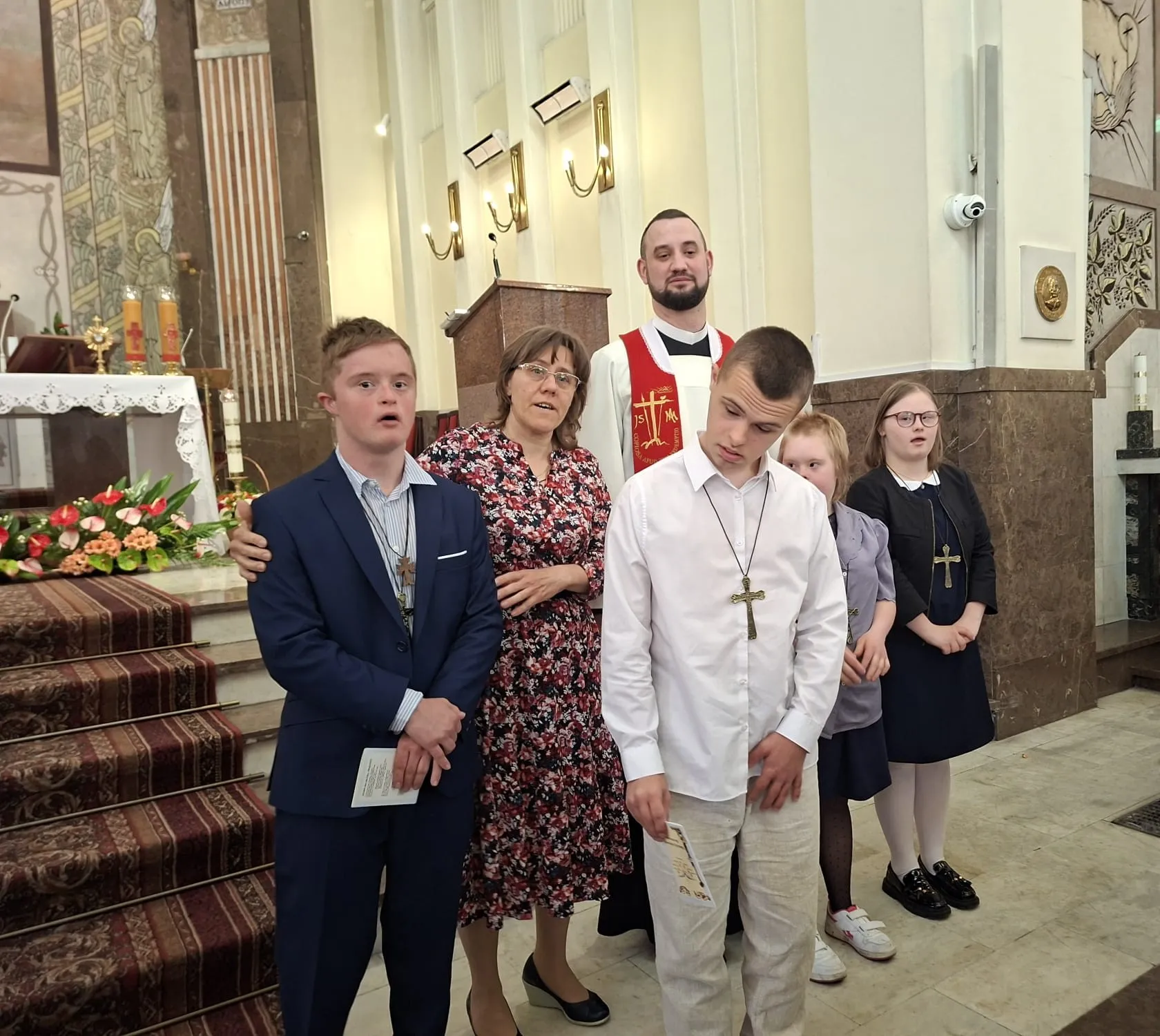Zdjęcie pamiątkowe - dwie uczennice i dwóch uczniów z klas starszych w wyjściowych strojach w towarzystwie księdza i pani katechetki stoją w kościele przed ołtarzem.