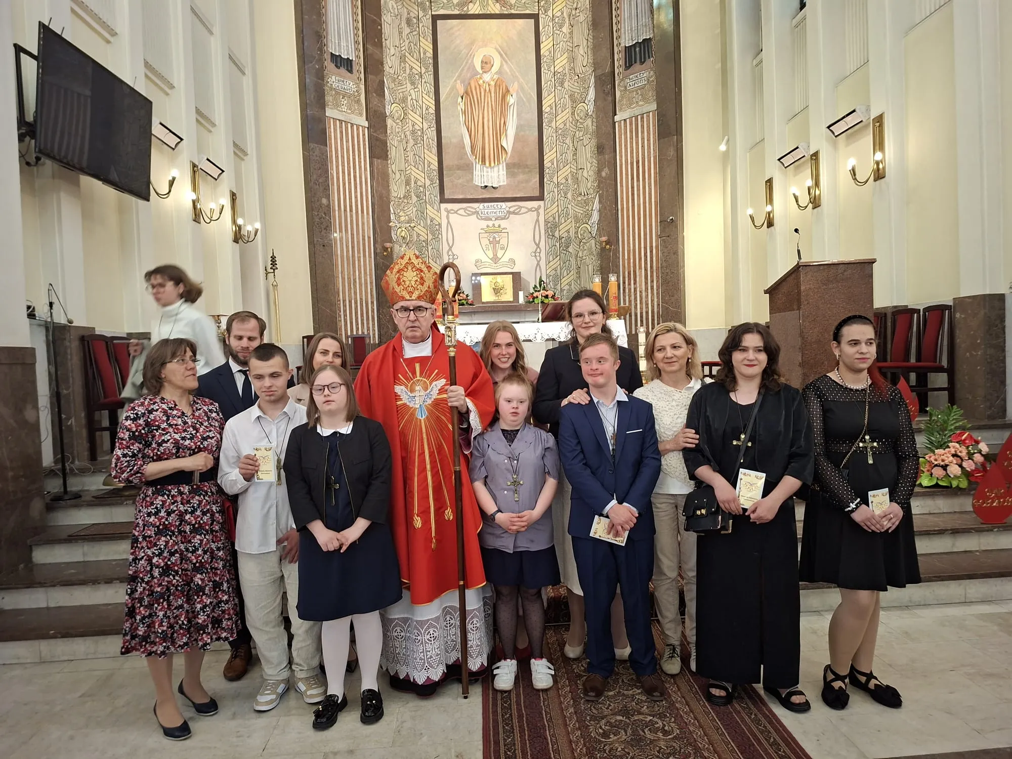 Zdjęcie pamiątkowe - grupa uczniów naszej szkoły w wyjściowych strojach w towarzystwie ks. biskupa, pani wicedyrektor szkoły, pani katechetki, pomocnika nauczyciela oraz członków rodzin dzieci stoją w kościele przed ołtarzem.                       