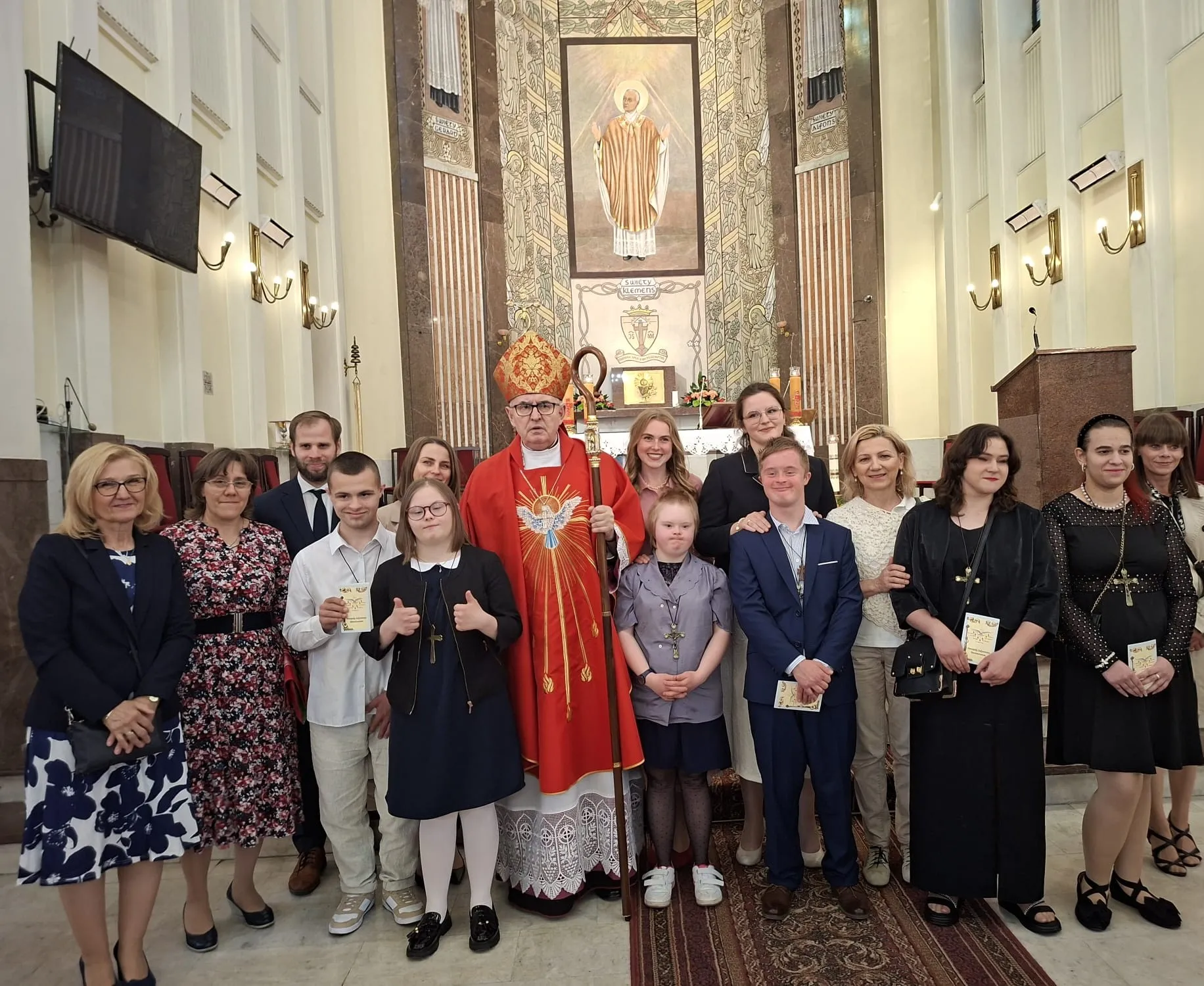 Pamiątkowe zdjęcie  - grupa uczniów naszej szkoły w wyjściowych strojach, w towarzystwie ks. biskupa, pani wicedyrektor szkoły, pani katechetki, pomocnika nauczyciela, członków rodzin dzieci stoją w kościele przed ołtarzem. 