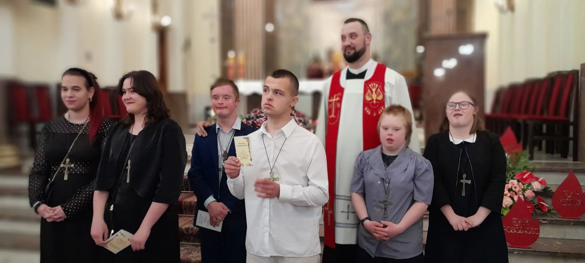 zdjęcie pamiątkowe - grupa uczniów naszej szkoły (sześcioro)  w wyjściowych strojach  w towarzystwie księdza stoją w kościele przed ołtarzem.