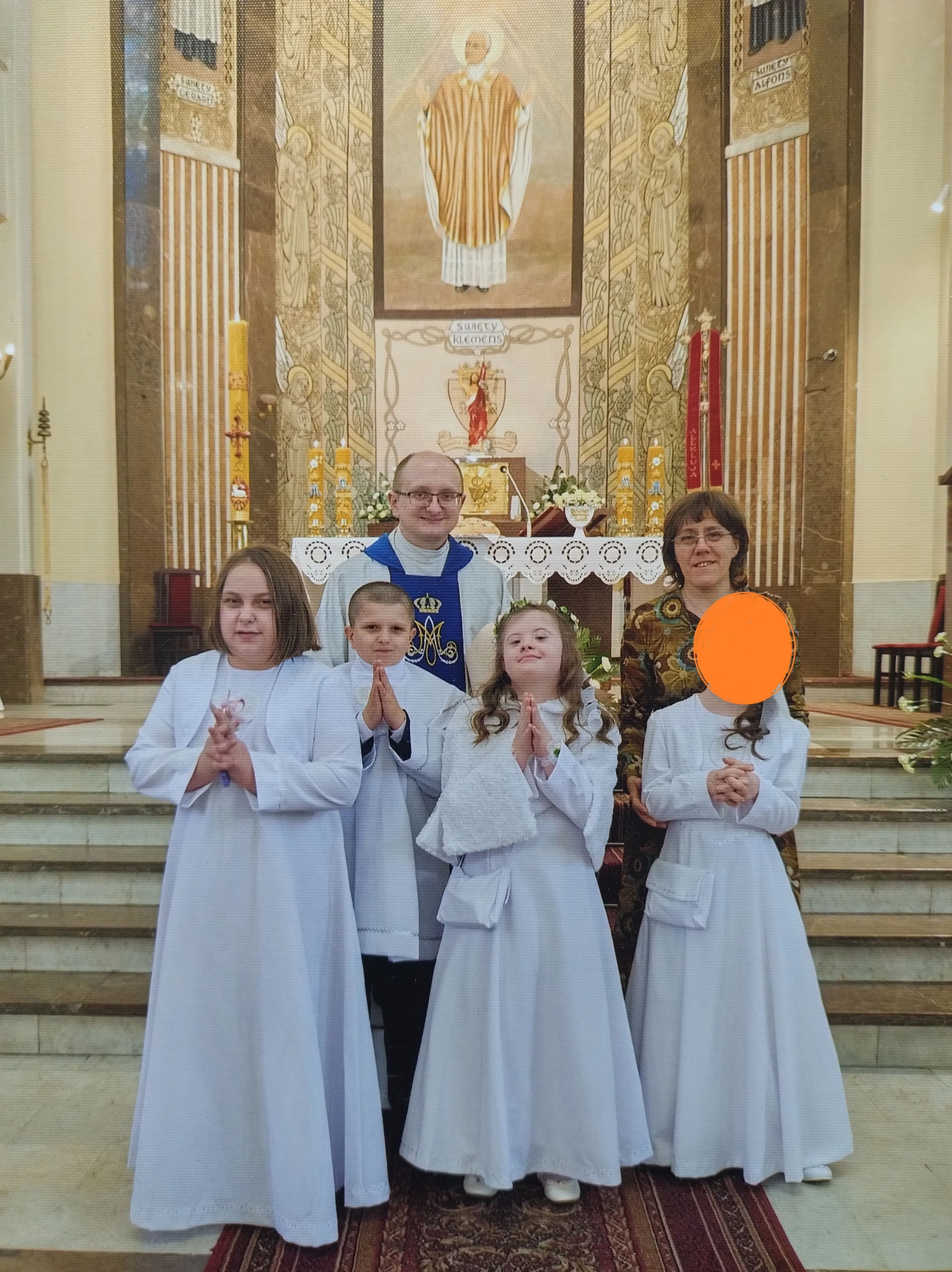 zdjęcie pamiątkowe - 3 uczennice i jeden uczeń w towarzystwie księdza  i pani katechetki stoją w kościele przed ołtarzem. 