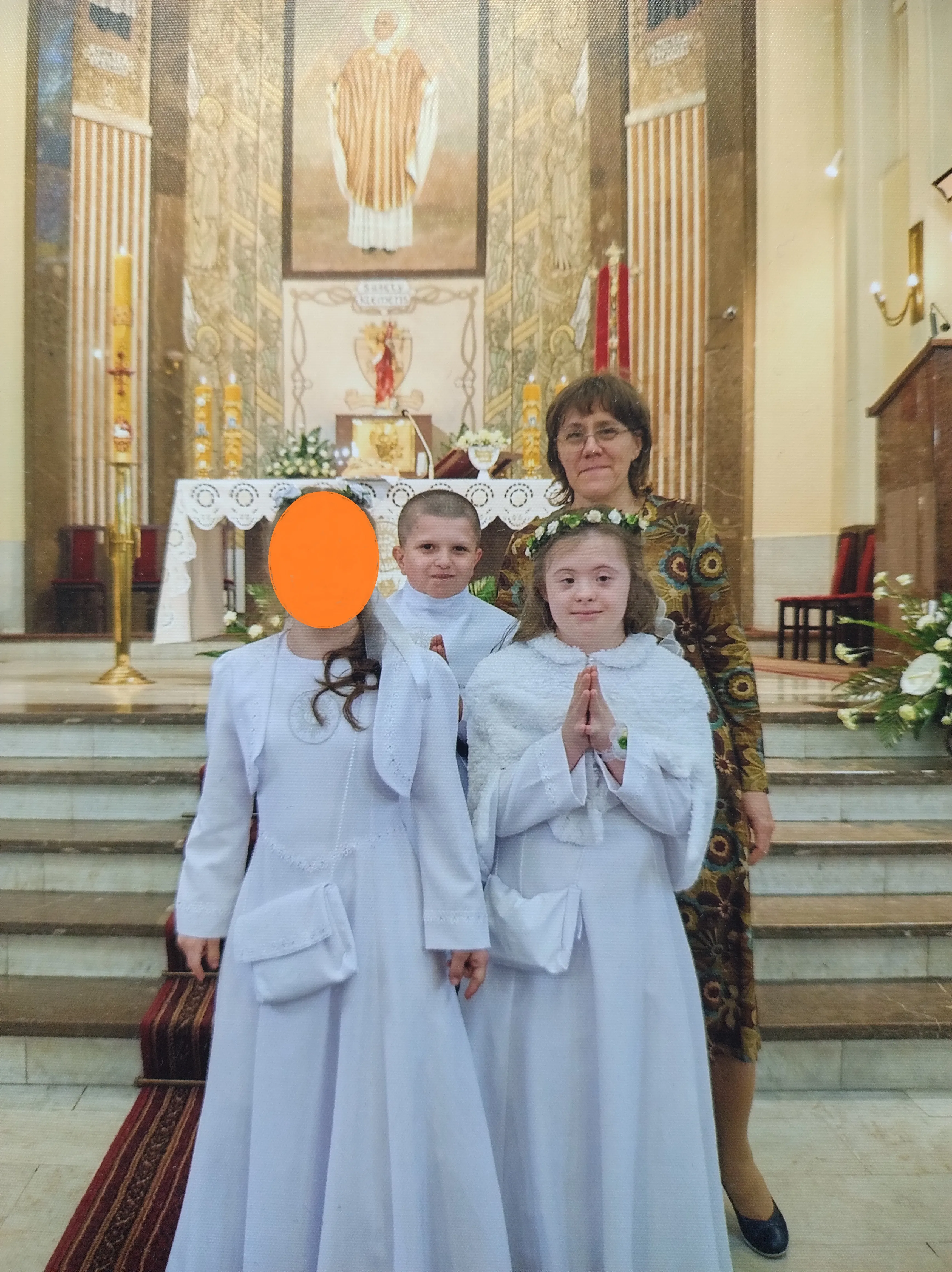 Pamiątkowe zdjęcie komunijne - dwie uczennice i uczeń w towarzystwie pani katechetki stoją w kośiele przed ołtarzem.